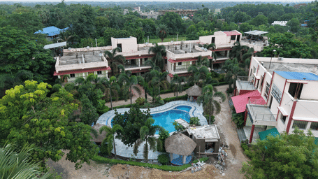 An aerial view of a swimming pool nestled among buildings and green trees at Shophori Wellness Retreat, Bolpur.
