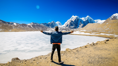 A person standing triumphantly on a snow-covered plateau surrounded by towering snow-capped mountains, celebrating adventure and exploration.