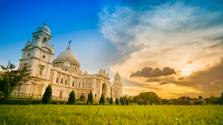 A stunning view of Kolkata’s iconic Victoria Memorial with its white domes glowing under the warm evening sky, surrounded by lush green lawns.