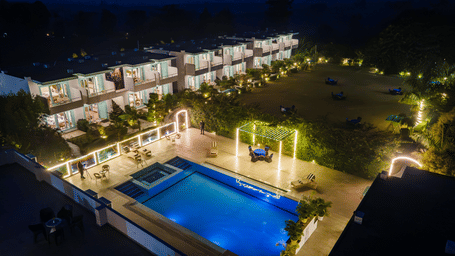Facade of Vedikant Resorts The Mallard Corbett at night featuring a swimming pool, lounger beds, chairs, tables, a huge lawn, and a two storey building with rooms.