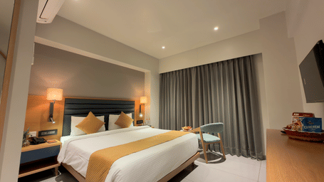 Hotel room with king size bed side tables, wall art, television, chair, desk, curtains, and window showing outdoor view