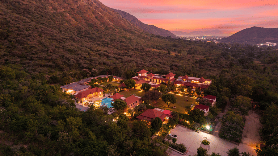 An elevated view of a luxury resort in Udaipur illuminated at dusk against a mountain backdrop | Anandam Jungle Retreat Resort
