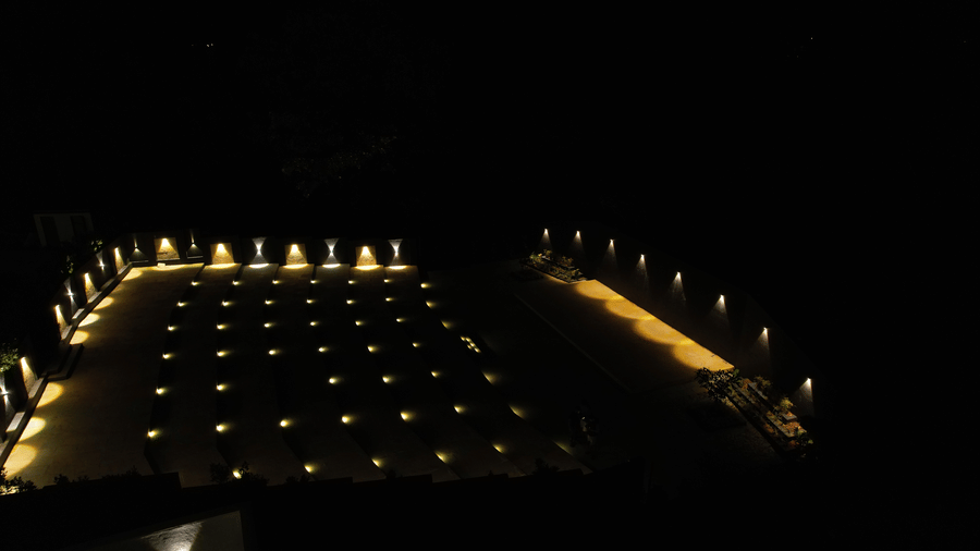 Dramatic night-time aerial view of an outdoor auditorium or seating arrangement, illuminated by small golden lights positioned in precise rows at Bindiga Peak Resorts.