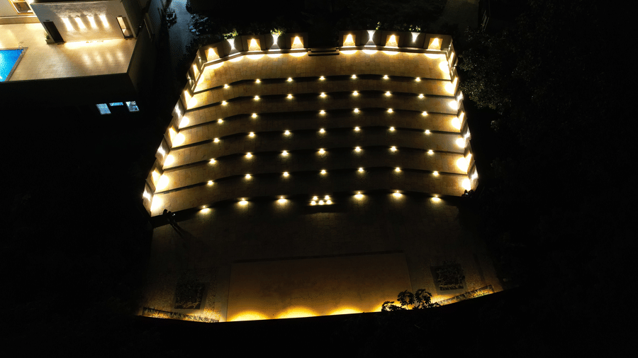 A modern amphitheatre glowing with golden tier lights against a pitch-black background at Bindiga Peak Resort.