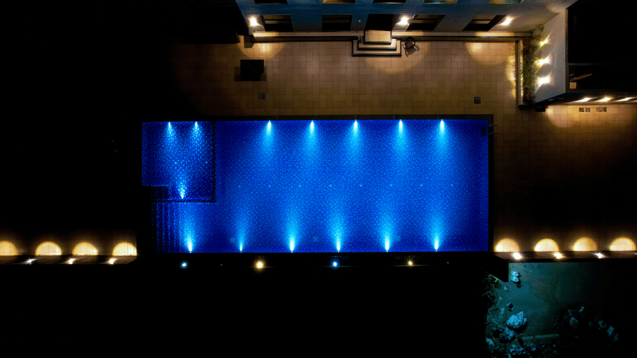 A rectangular swimming pool glowing with bright blue underwater lights at night at Bindiga Peak Resort.