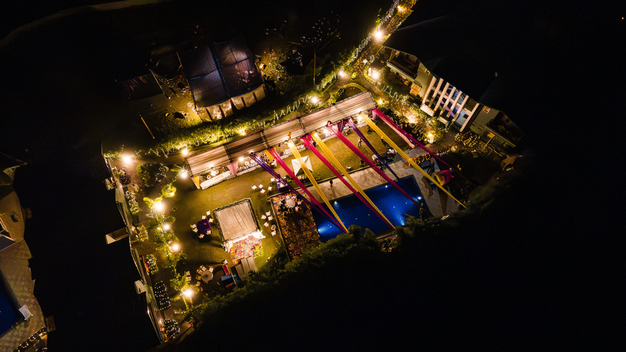 Aerial view of a night-time event setup at Corbett Nirvana Resort on a large lawn, showing the area brightly illuminated with fairy lights and decor.