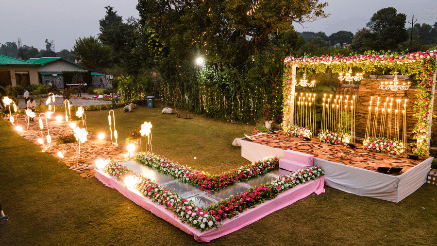 Night-time view of an outdoor event setup at Corbett Nirvana Resort with a decorated frame, surrounding floral boxes, and ground-level lighting.