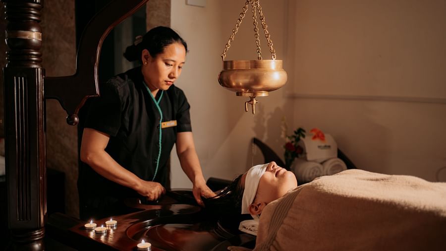 A woman offering an oil relaxation treatment to a guest reclining on the bed at Crescent spa & resort, Indore