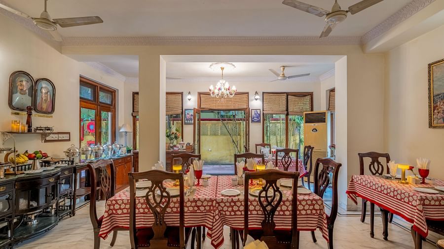 A spacious dining room with set tables, wooden chairs, ceiling fans, and a glimpse of an adjoining room | Dera Rawatsar, Jaipur