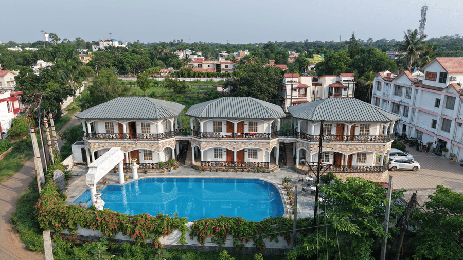 A daytime aerial view of Dip Holidays Resort showing 3 connected 2-storey accommodation buildings next to a swimming pool and trees.