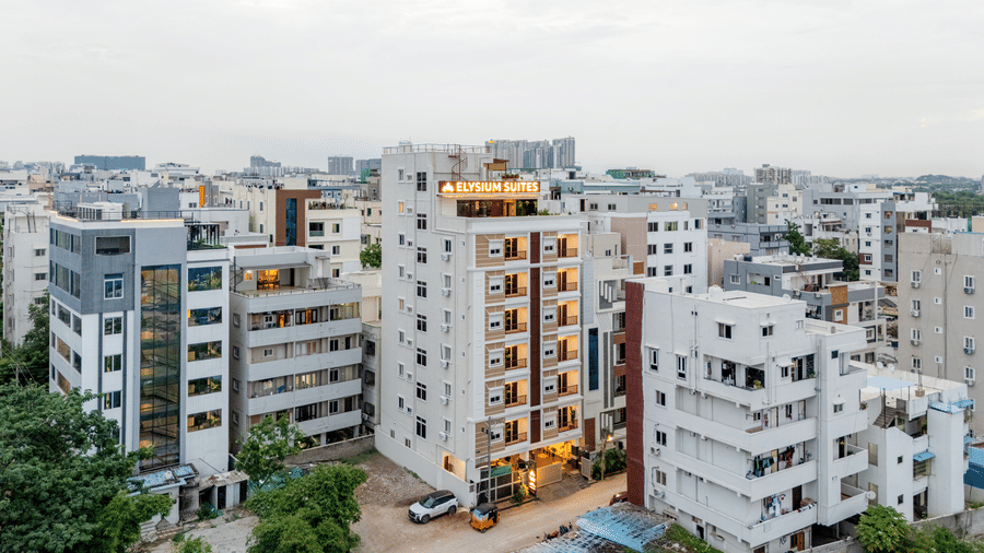Buildings stand close together in a city under a bright sky with lights visible from windows near Elysium Studio Suites, Madhapur.