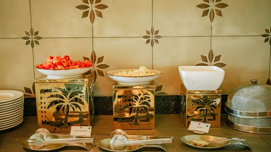 Breakfast counter with cereal dispensers, fruit bowls, and cutlery placed neatly on a tiled wall backdrop at Fireflies Resorts, Kabini.