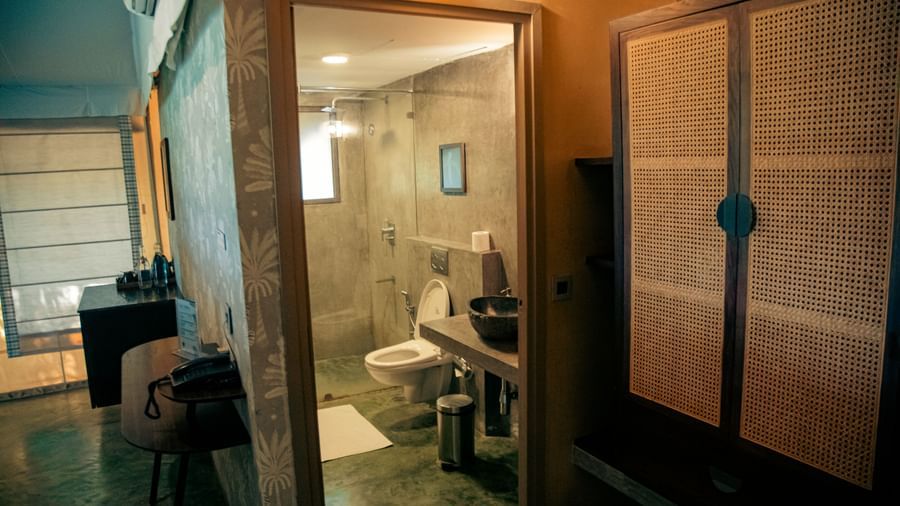 Bathroom with glass door shower area, white toilet, partially visible rack, and mirror at Fireflies Resorts, Kabini.