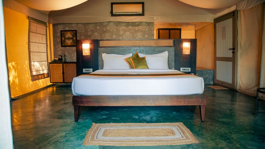 Bedroom with king size bed, green floor, two yellow cushions, nightstands with lamps, and a rug at Fireflies Resorts, Kabini.