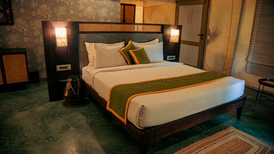 King size bed with mustard cushion, bedside lights, and green floor at Fireflies Resorts, Kabini.