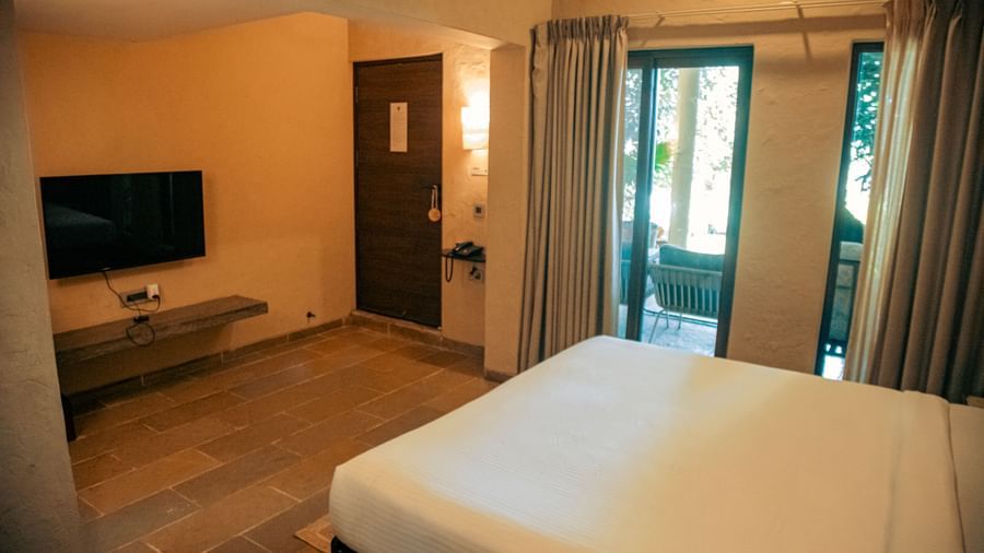 Room with a mounted TV, and a king size bed featuring glass doors leading to a balcony at Fireflies Resorts, Kabini.