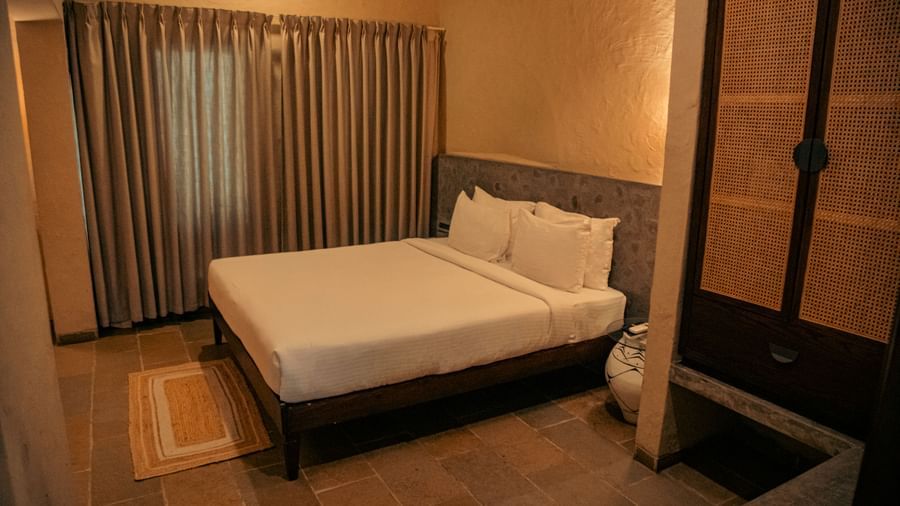 Bedroom with a king size bed, neutral furnishings, wooden flooring, and a large curtain at Fireflies Resorts, Kabini.