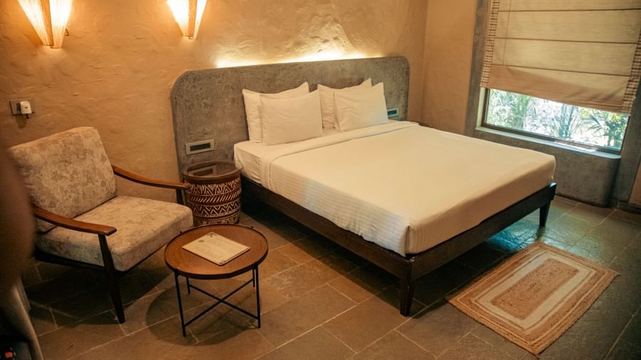 Room with a king size bed, two chairs, a round side table, and beige walls at Fireflies Resorts, Kabini.