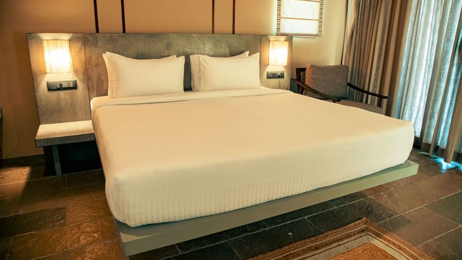 Bedroom with king size bed, bedside lamps, floor rug, and sheer curtains covering a glass window at Fireflies Resorts, Kabini.