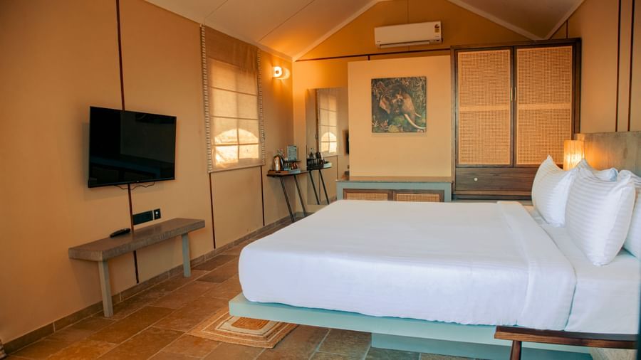 Room with a king size bed, mounted TV,  bedside lamps, and beige panelled walls at Fireflies Resorts, Kabini.