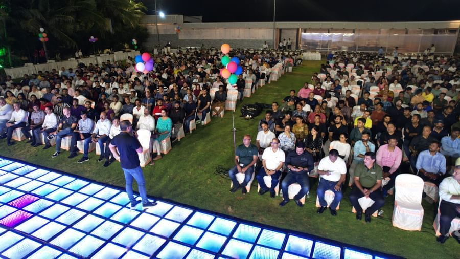 An outdoor corporate event held at Grande Bay Resort & Spa featuring people seated in chairs and a person on a grid structured stage.