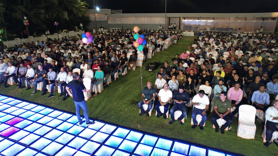 A night event featuring a speaker on an LED-lit stage with a large seated audience spread across an outdoor lawn - Grande Bay Resort & Spa, Mamallapuram