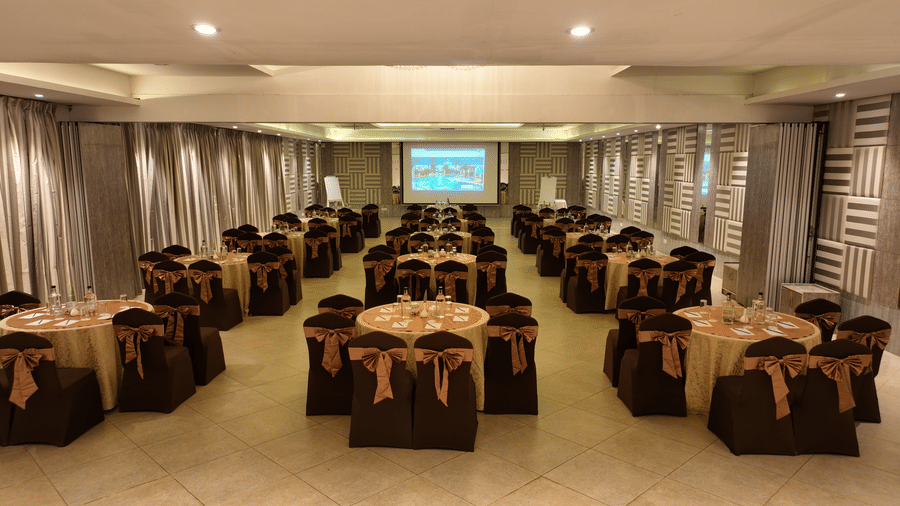 Banquet hall with brown chair covers arranged around round tables at Grande Bay Resort & Spa, Mamallapuram.