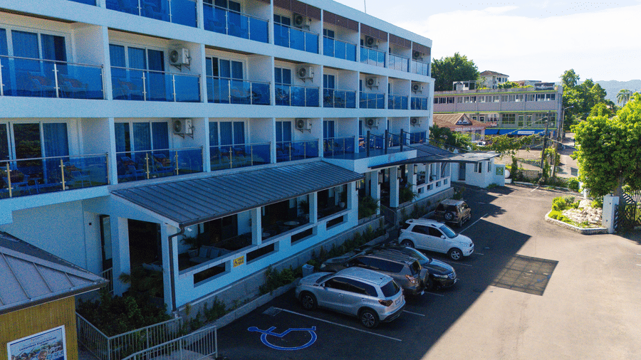 Facade of Hotel 39 in Jamaica with cars parked in front of it on a sunny day