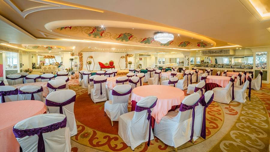 Samrat featuring round tables draped in pink tablecloths and chairs adorned with white covers and purple sashes.