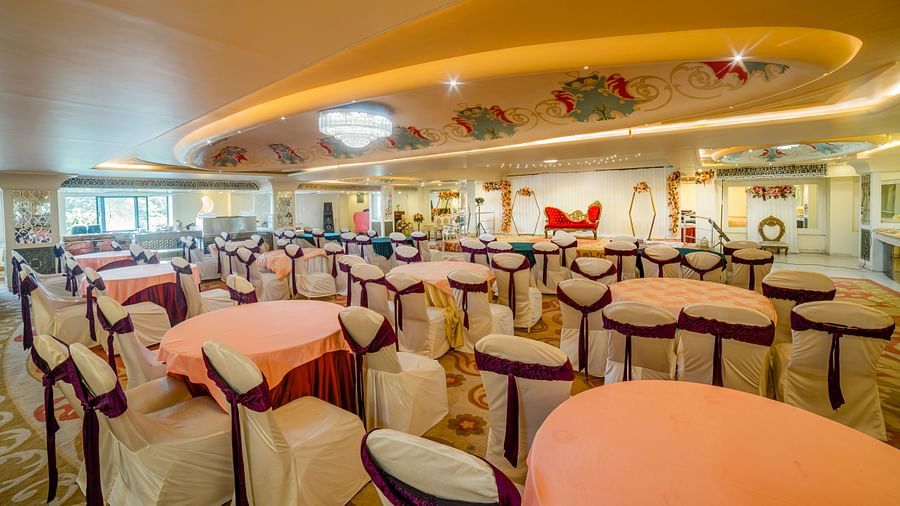 Samrat featuring round tables with pastel-colored tablecloths and cushioned chairs, under warm lighting and decorative ceiling elements.