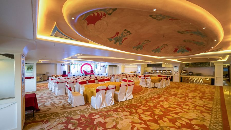Samrat featuring a patterned carpet, round tables with chairs, and a stage area.