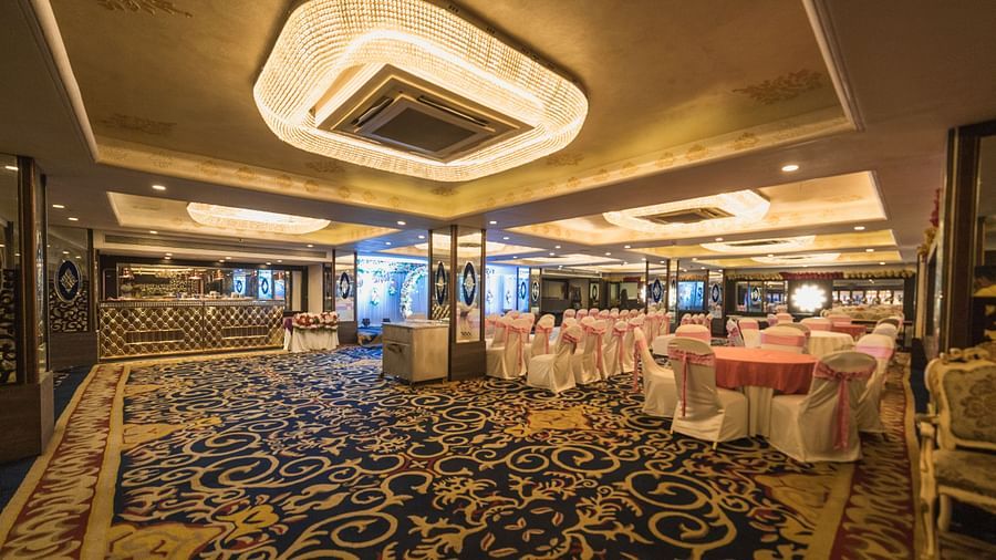 Magadh with round tables, chairs with covers, patterned carpeting, and decorative lighting fixtures on the ceiling.