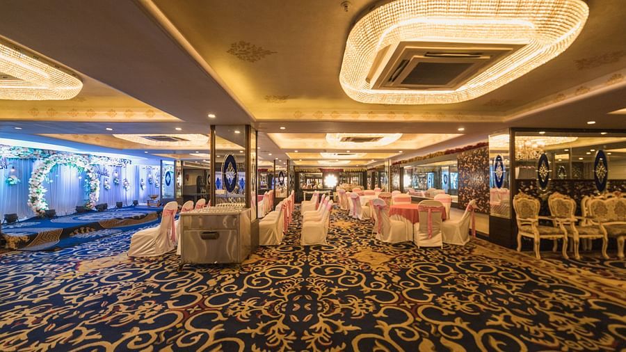 Magadh with a patterned blue carpet, tables set with white linens, and modern lighting fixtures.