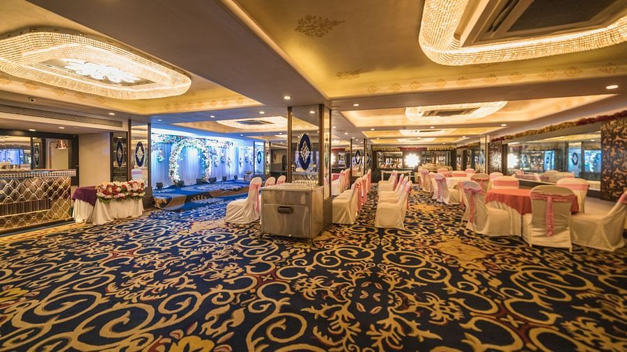 Magadh featuring shows tables draped in white cloths, chairs with pink accents, and a patterned blue carpet.