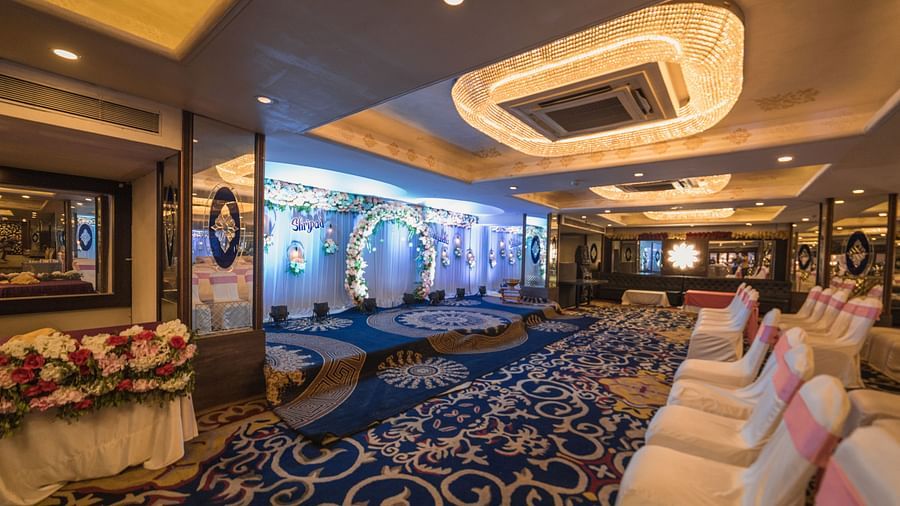 Magadh showcasing blue patterned carpeting, chairs with pink and white covers, and modern ceiling lights.