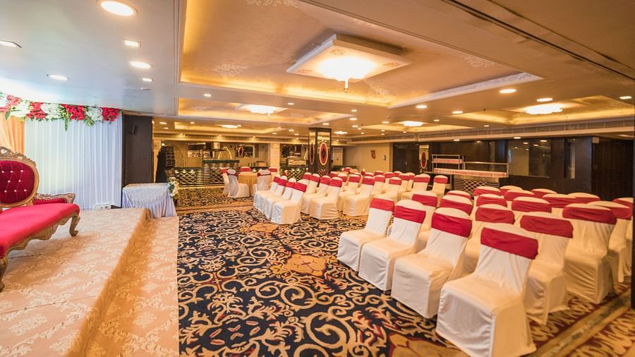 Maurya featuring rows of chairs covered in white fabric and red sashes, and a patterned carpet.