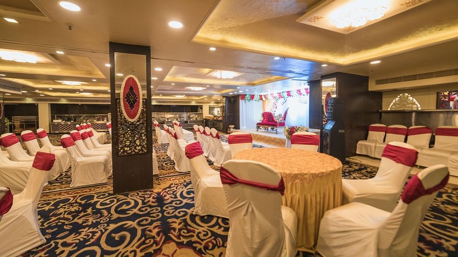 Maurya featuring round tables covered in beige cloths and white chairs, highlighting the room's carpet and pillars.