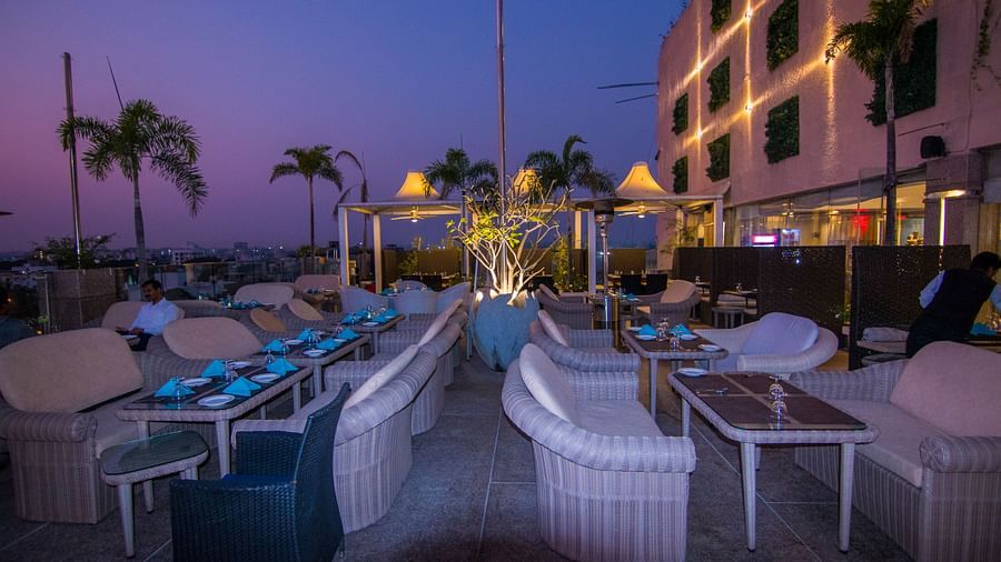 An outdoor dining setup at Hotel Ashok Nagpur with white cushioned chairs and small tables arranged for guests.