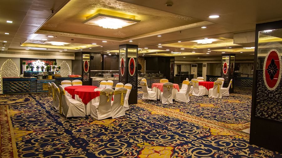 Maurya featuring round tables draped in red cloths and surrounded by white chairs, featuring a patterned carpet and decorative pillars.