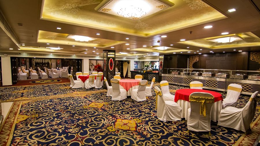 Maurya featuring round tables covered in red cloths and surrounded by white chairs, under a well-lit ceiling and patterned carpet.