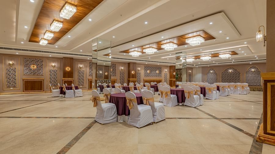 Banquet hall at Hotel Highway King, Bagru, with decorated tables and chairs, wooden accents, and elegant ceiling lighting.