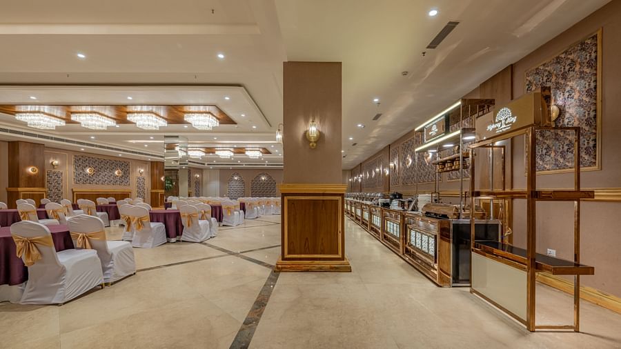Banquet hall at Hotel Highway King, Bagru, featuring decorated chairs, wooden paneled walls, and elegant lighting fixtures.