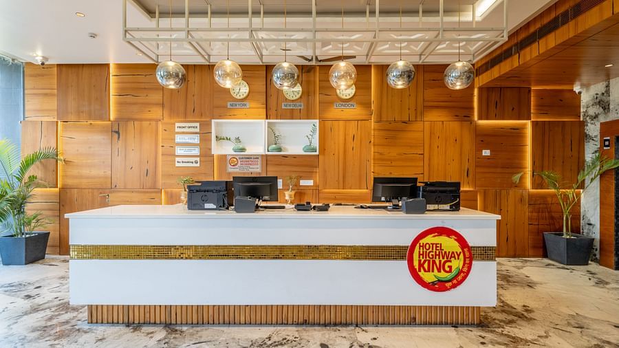 Reception desk at Hotel Highway King, Bagru, with computer stations, wooden paneled walls, and hanging light fixtures.