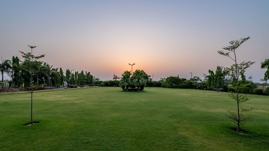An extended view of the expansive open garden area in the premises of Hotel Highway King, Behror, seen with trees, and grass.