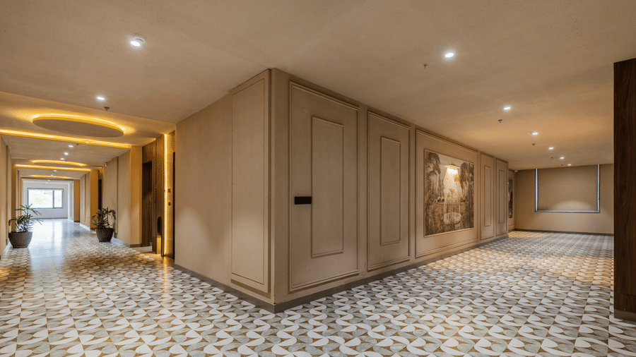 A wide corridor junction with a decorative patterned tile floor, smooth wall panels, and warm recessed ceiling spotlights at Hotel Highway King, Harmada.