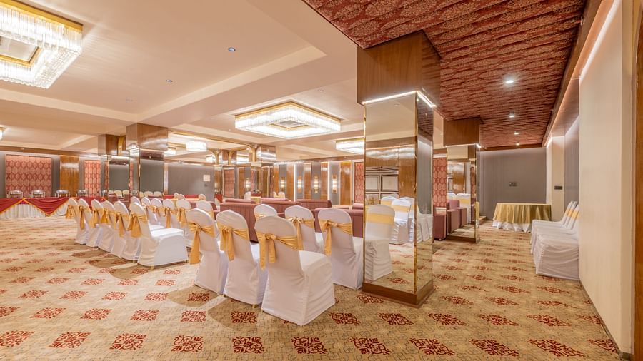 Banquet seating with white-covered chairs tied in gold sashes arranged around a stage setup at Hotel Highway King, Jaipur.
