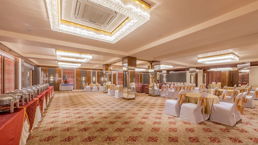 A wide banquet hall with patterned carpet, ceiling lights, and a mix of tables and sofas set for an event at Hotel Highway King, Jaipur.