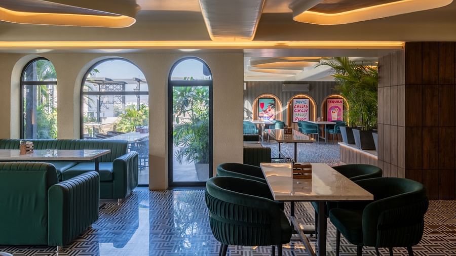 Dining area with green chairs, arched windows, and wall posters at Hotel Highway King, Jaipur.