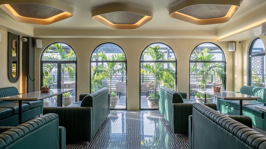 Lounge dining set up with arched windows, green sofas, and ceiling lights at Hotel Highway King, Jaipur.