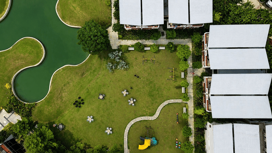 An aerial top view of Hotel Sonar Bangla, Mayapur, featuring lawn areas, outdoor furniture, a water body, and building roofs.